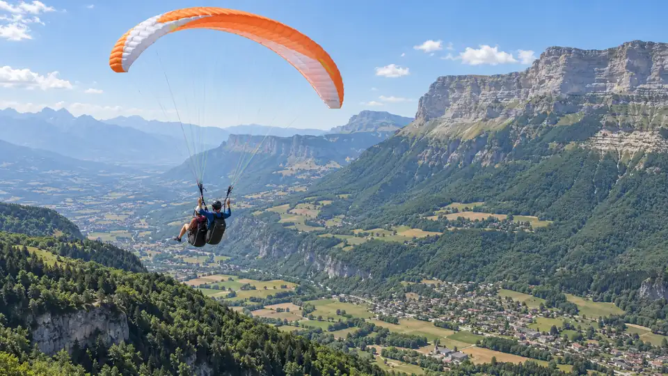 Parapente biplace devant des falaises et une vallée de la Chartreuse.